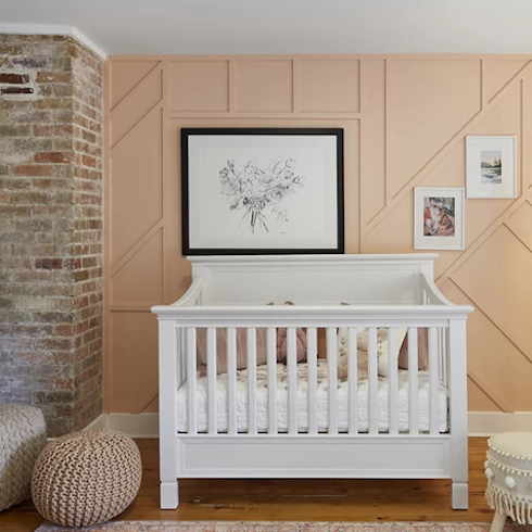 Beautiful nursery with a white crib, two woven floor poufs, an exposed brick chimney and a panelled wall painted a pretty peach colour.