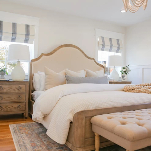 Beautiful white bedroom with wooden bed and side dressers, white painted walls, and white and blue striped roman blinds.