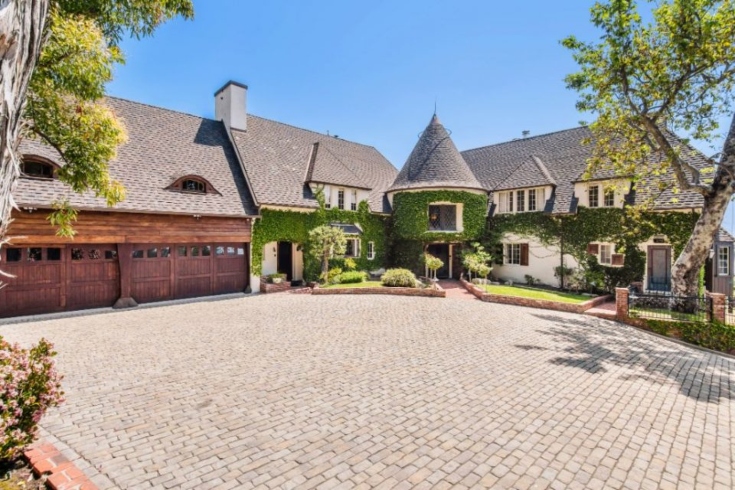 The white storybook-style house built in the 1930s by Walt Disney has a turret, a cobblestone driveway, stained glass windows, and vines covering the exterior.