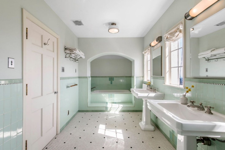 A master bathroom with vintage tiled floors, mint green tiled walls, dual sinks, and a bathtub