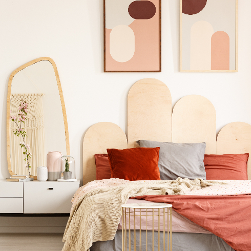 Image of a king-size bed standing next to a shelf with a mirror in a bedroom interior with two posters on a wall