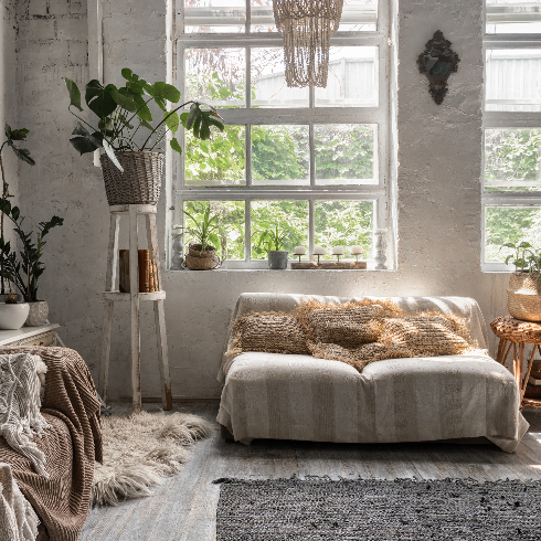 Lounge room with stylish interior design at comfortable house, sofa, cushions, soft plaid, house decor and green plants in flower pots near mirror on commode