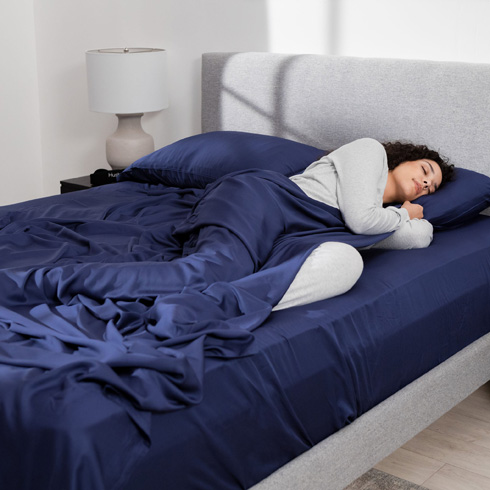 Woman sleeping on dark blue sheets on a gray bed.