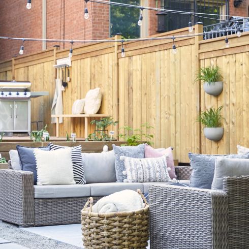 Small backyard with hardscaping, modern grey couch and string lights.