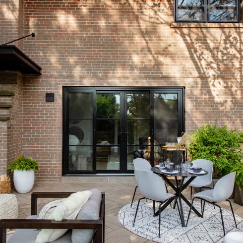 Small backyard with small dining table and grey chairs, along with comfy lounge chair and plants.