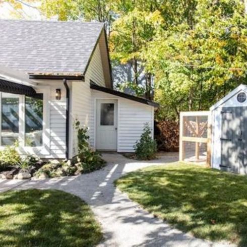 Small backyard with grass and paved path, modern white shed and minimalist landscaping.