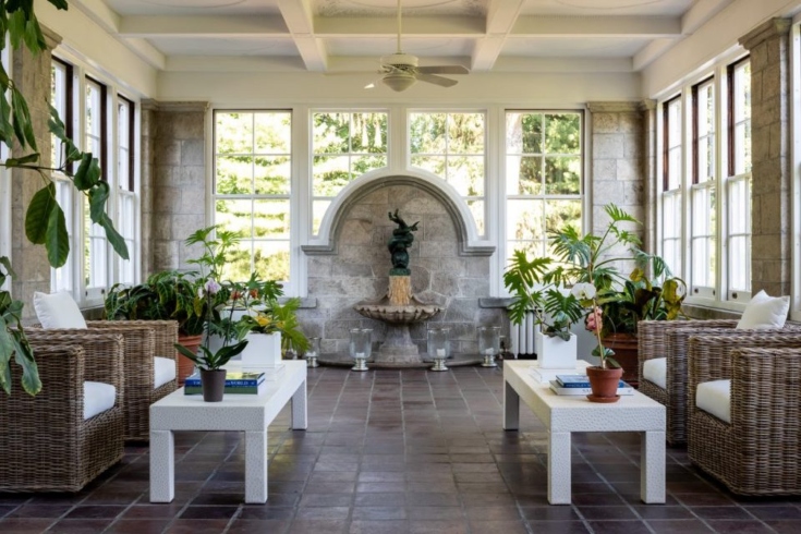 A sun room with seating, end tables and large windows