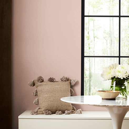 A small dining nook with bench seating, round table, a large window and sandy-toned walls