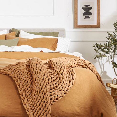 Bedroom with burnt orange sheets and cozy throw with white aesthetic