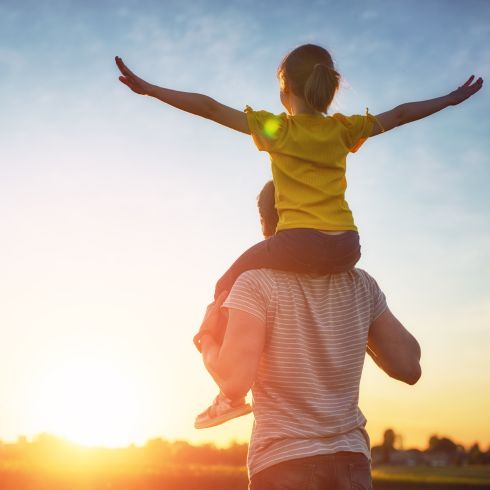 father outside with daughter on shoulders looking out into the sunset