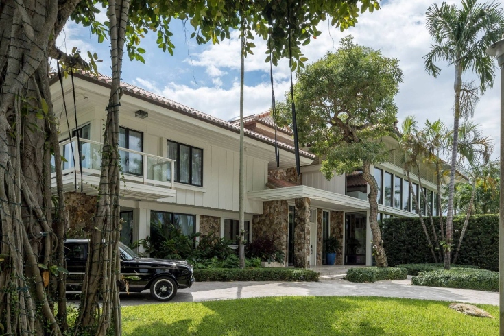 The exterior of a mansion with stonework around the entrance, large windows, beige siding and terra cotta roof