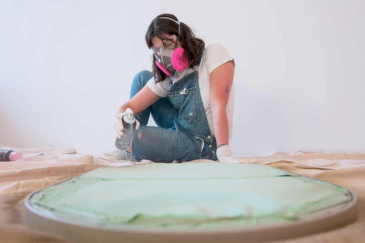 DIY expert Maca spray painting a bathroom mirror using metallic spray paint from Behr
