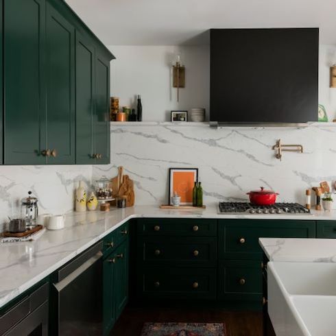 Dark green shaker style cabinets with gold hardware and grey veined white marble countertops and backsplash feature in a chic kitchen renovation by Kortney Wilson for Home Network