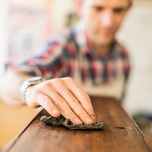 an older white man in the background; hand wiping hardwood antique with a dry cloth in foreground