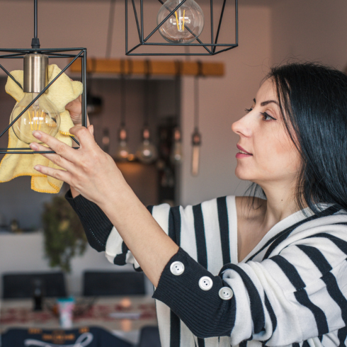 an older white woman dusting her hanging light fixture with a dry cloth