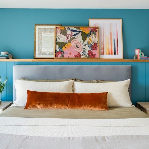 A bright blue bedroom with a white bed and pictures on the wall