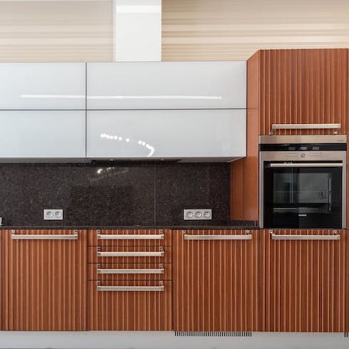 A sleek wall of kitchen cabinets with white upper cabinets and fluted wood cabinets