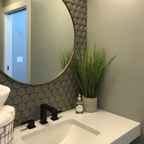 A modern bathroom with grey wall tiles and a round mirror over the sink