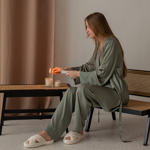 Woman in Satin Pyjamas Sitting and Lighting a Candle on Coffee Table