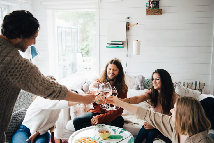 a group of friends clinking wine glasses over a table while seated on a couch