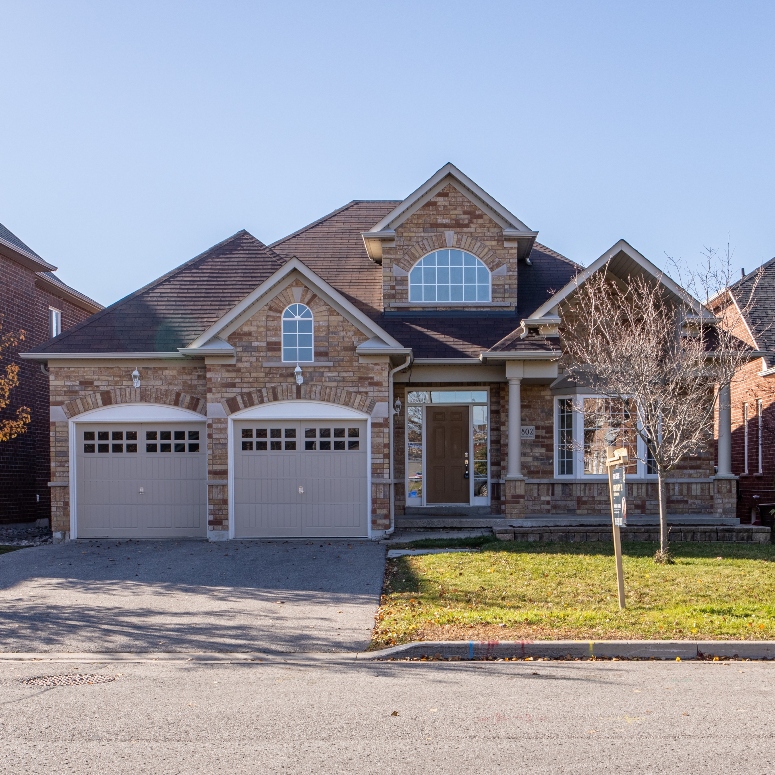 A detached house with two garages and a for sale sign on the lawn