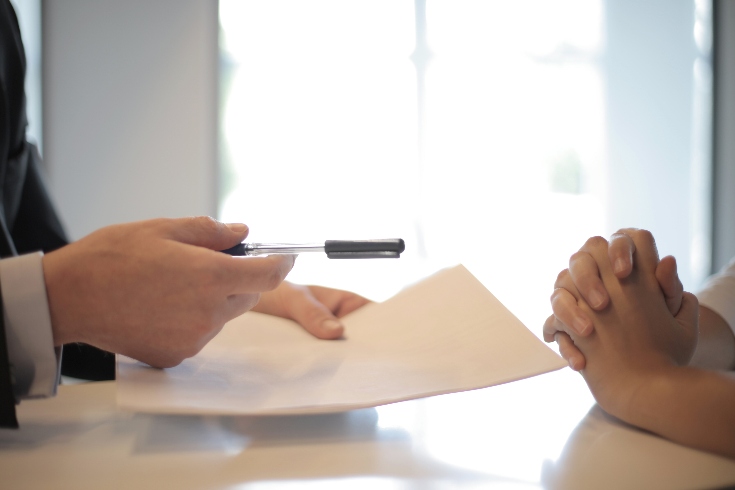 Someone passing paperwork and a pen across a desk to another person