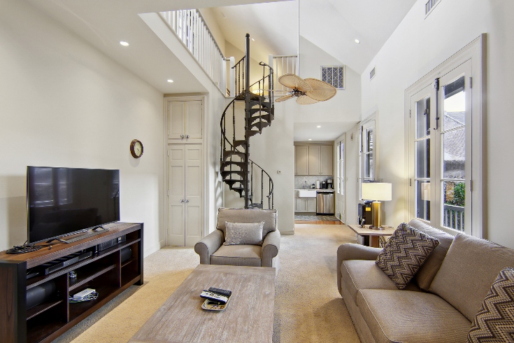 A guest house living room with sofa, TV, spiral staircase and doors leading to a balcony.