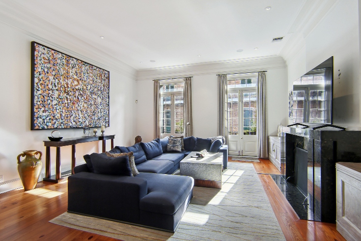 A formal living room with dark blue sectional sofa, marble fireplace, and double French doors.