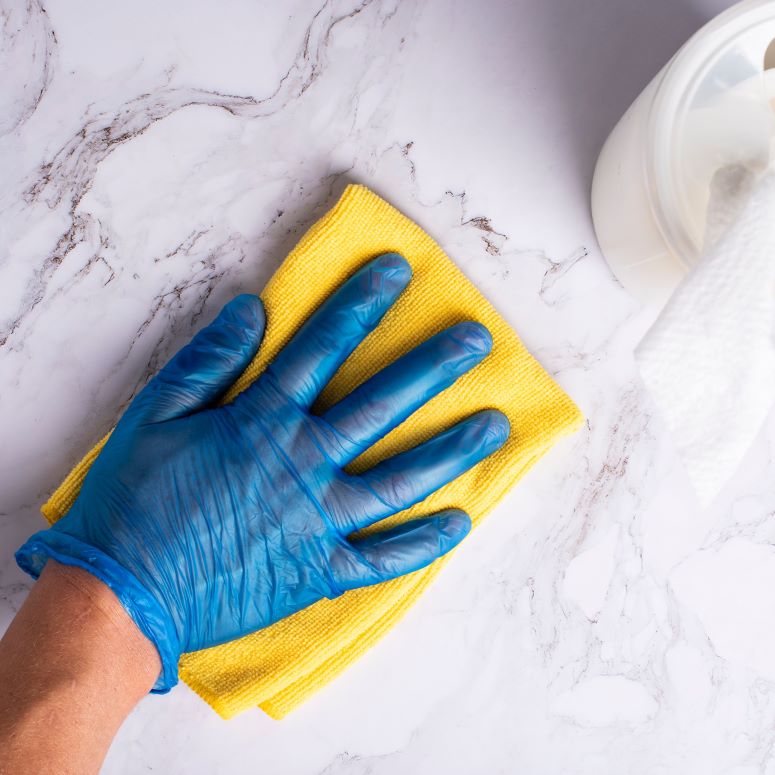 A blue gloved hand using a yellow sponge