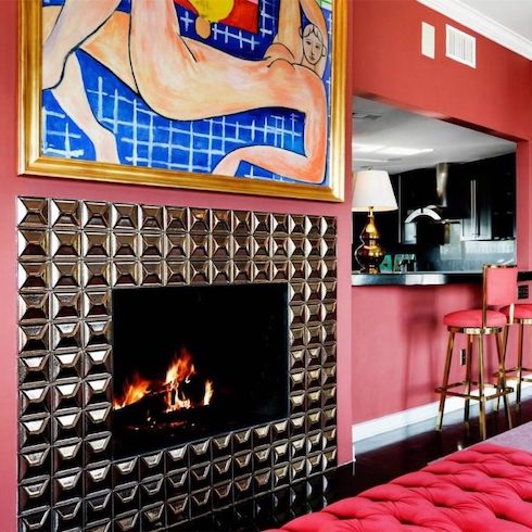 Funky pink living room and bar area featuring a metallic tile fireplace, a gold framed abstract painting above it, pink and gold bar stools, black flooring and a pink tufted bench