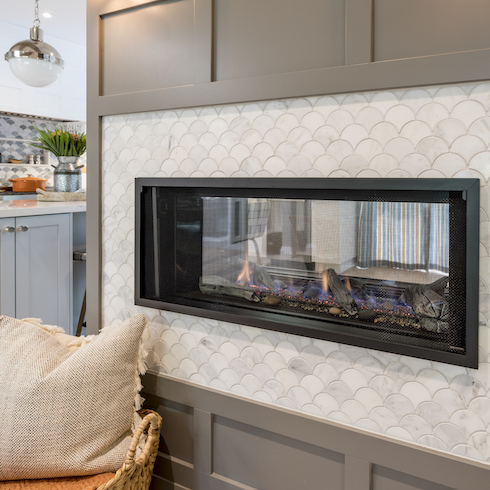 See-through gas fireplace with white scallop tiles and brown panelling divides the kitchen and the dining room in a remodelled home featured on Home Network