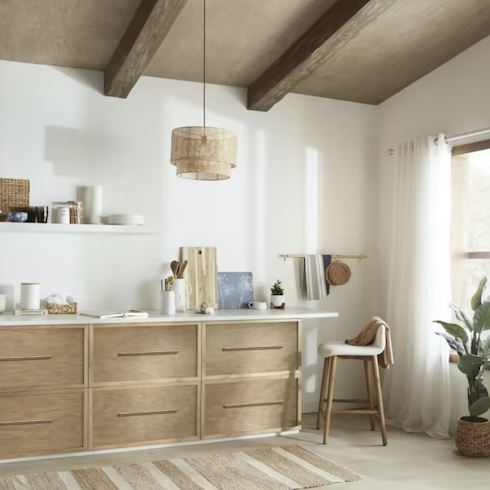 Wood and rattan Ceiling Lamp by Bouclair featured in Home Network’s kitchen lights gallery in a chic kitchen with wood lower cabinets, white countertops, a white floating shelf, a white and wood stool, and a brown ceiling with two exposed wood beams