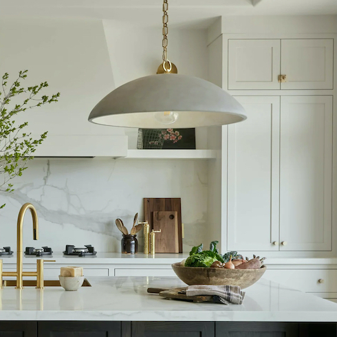 Elliot Pendant by Light House featured in Home Network’s kitchen lights gallery in a modern kitchen with a large centre island with a sink, soap bowl, and a large stone bowl filled with vegetable, marble countertops and backsplash, white cabinets and large stove fan hood, gold hardware, cutting boards, grinders and a spoon pot on the counter