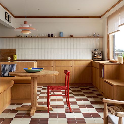 Louis Poulsen PH 5 Pendant from Finnish Design Shop featured in Home Network’s kitchen lights gallery shown in a colourful Helsinki kitchen and breakfast nook with brown and white floor tiles, wooden lower cabinets, white tile backsplash, a wooden floating shelf holding glassware, and a built-in eat-in bench, round kitchen table and a red chair