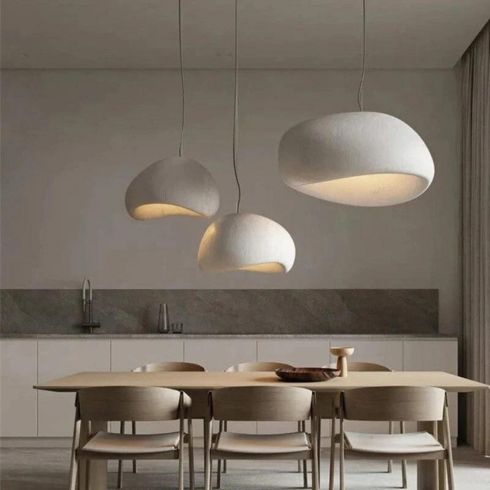 Three Khmara Wabi-Sabi Pendant Lights featured in Home Network’s kitchen lights gallery shown in a chic kitchen with brown and white stone countertops and backsplash, ash wood cabinets, a cutting board with bread and a rolling pin, two wooden stools, and under cabinet lighting