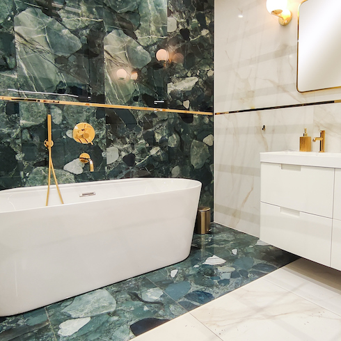 Bathroom interior with white standalone bathtub, floating vanity and sink, cream coloured ceramic tile walls, statement stone splash wall, and gold hardware shown in the Home Network gallery Unusual Bathroom Renovation Ideas That Will Be Popular In 2025