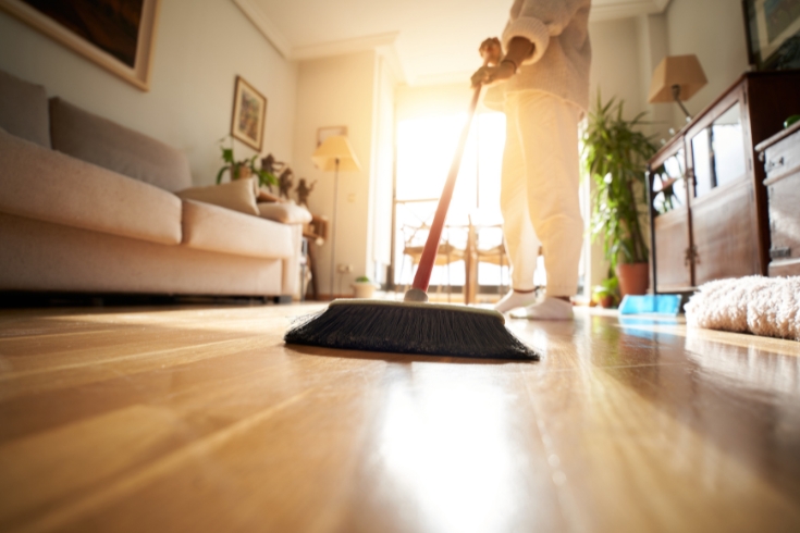 Person sweeping the parquet floor, window light reflection. 