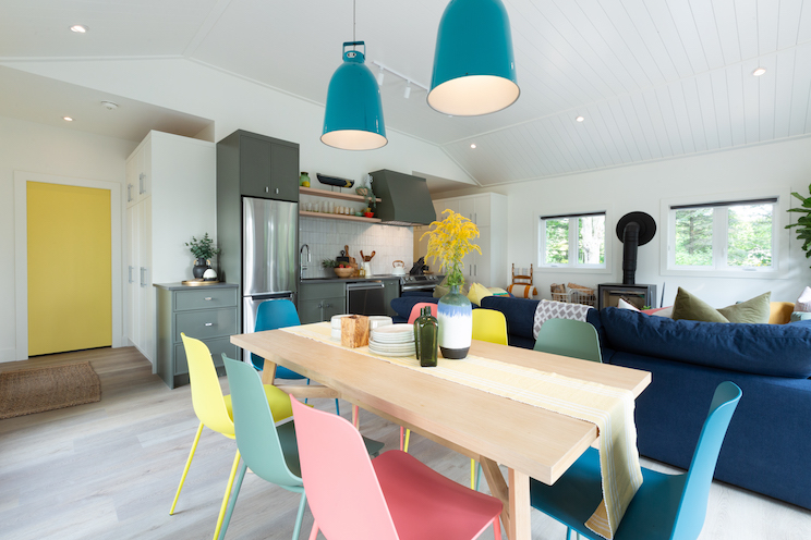 Wood table and colourful chairs next to open concept kitchen