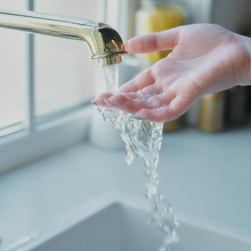 A kitchen tap with the water on and a hand feeling the temperature