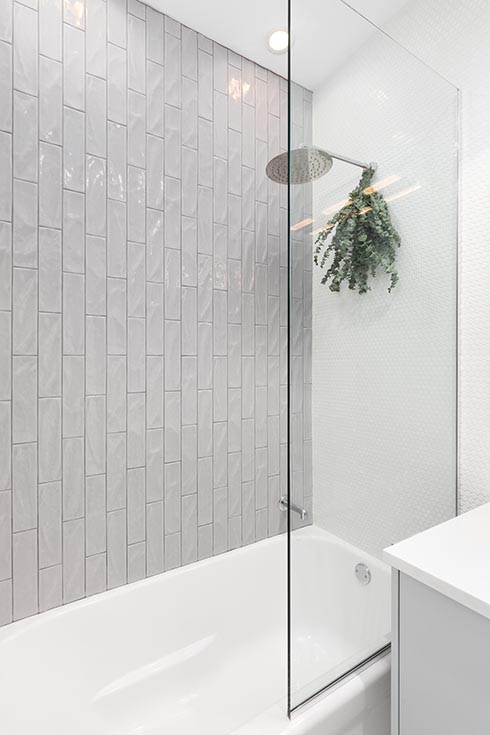 A shower detail with grey vertical subway tiles, white...