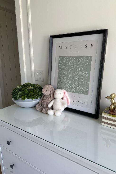 A picture frame, plant and two bunnies on a dresser