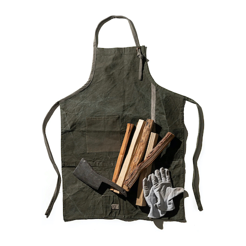 Puebco Vintage Tent Fabric Apron on a white background with a hatchet, kindling and leather work gloves as part of HGTV Canada's 10 Gift Ideas for the Men in Your Life