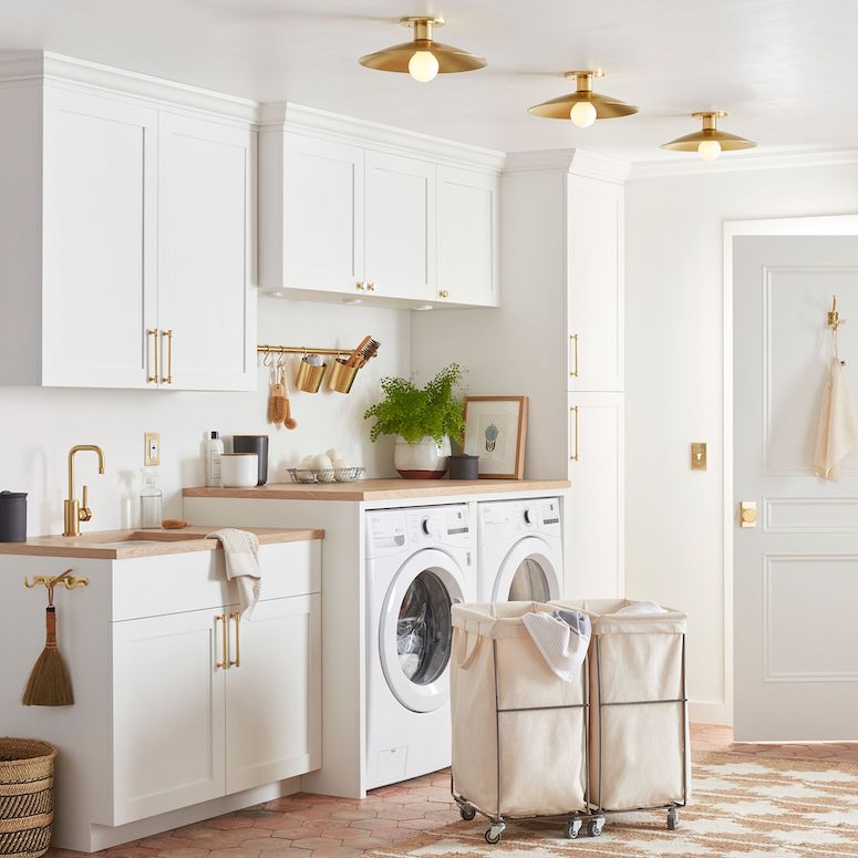 Beautiful laundry room with white cabinets, gold hardware and tile floors as featured in Laundry Mistakes on HGTV Canada featuring Rejuvenation Steele Canvas Laundry System
