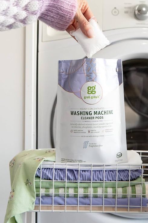 Grab Green Washing Machine Cleaning Tabs as featured in Laundry Mistakes on HGTV Canada sit on a pile of clean laundry with a hand above