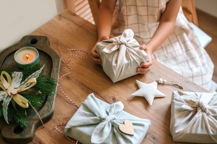 More Sustainable Holidays featuring a wooden table with a pair of children's arms holding a cloth wrapped present