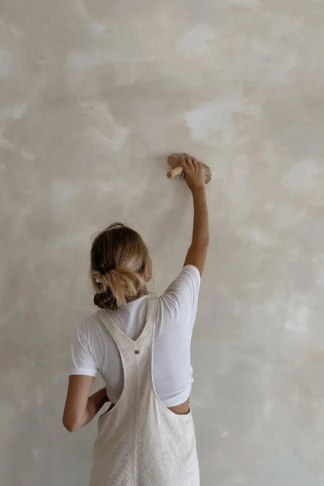 An image of a woman painting a wall with limewash paint in a neutral cream