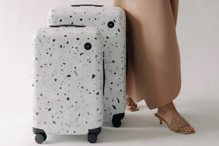 Monos Terrazzo Carry On cases on a white floor in front of a woman wearing tan pants and kitten heels Home Network Best Carry-On Luggage