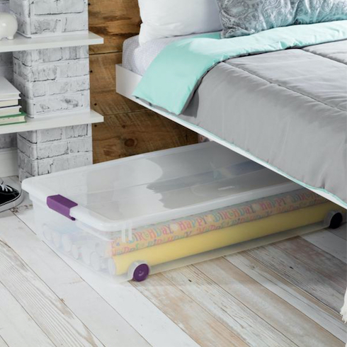 Sterilite ClearView Wheeled Underbed Storage Box half tucked under a bed on grey wood floors as part of Home Network The Secret to Storing Holiday Decorations in Small Spaces