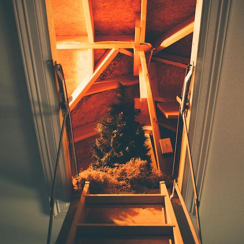 View up a ladder to an attic with an artificial Christmas tree as part of Home Network The Secret to Storing Holiday Decorations in Small Spaces