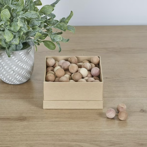 Neatfreak! Natural Cedar Balls sit on a wood floor beside a cedar branch in a grey pot